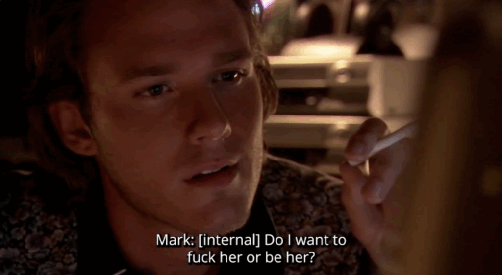 A screenshot of a white man smoking and looking intensely at a computer screen, with a subtitle that reads, "Do I want to fuck her or be her?"