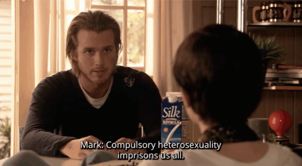 A white man sitting at a table. The subtitle text reads, "Compulsory Heterosexuality imprisons us all"